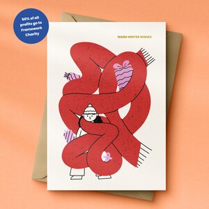 May include: A festive greeting card with a red scarf design and the text "Warm Winter Wishes" in gold. The illustration shows a person in a white hat and mittens, embraced by a large red scarf. A blue circle indicates that 50% of profits go to Framework Charity.