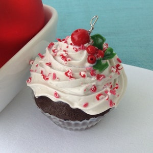 May include: A white chocolate cupcake with red and white sprinkles, topped with a red candy and green holly leaves.