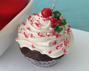 May include: A white chocolate cupcake with red and white sprinkles, topped with a red candy and green holly leaves.