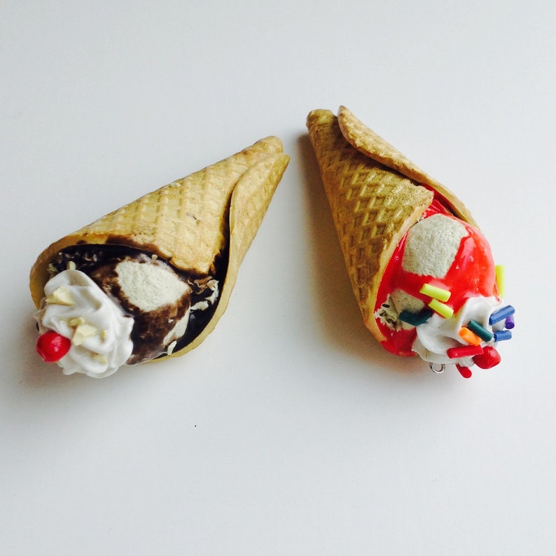 May include: Two miniature ice cream cones, one with chocolate and vanilla ice cream and the other with red and white ice cream with sprinkles.