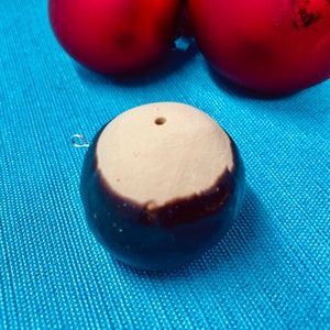 May include: A round, brown and white ornament with a small hole at the top. The ornament is sitting on a blue surface.