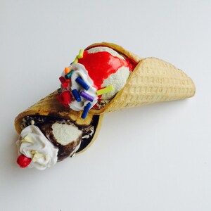 May include: Two scoops of ice cream in a waffle cone. One scoop is vanilla with red sauce and sprinkles, the other is chocolate with whipped cream and a cherry.