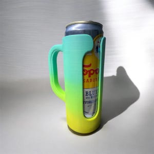 May include: A teal, green, and yellow gradient can holder with a handle, holding a can of Topo Chico Blue. The can holder is made of plastic and has a modern design. The can is visible through the holder's opening.