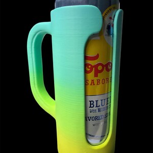 May include: A gradient-colored can cooler in shades of green and yellow, designed to hold a standard beverage can. The cooler has a handle for easy carrying and a snug fit to keep drinks cold. The can inside is yellow and blue.