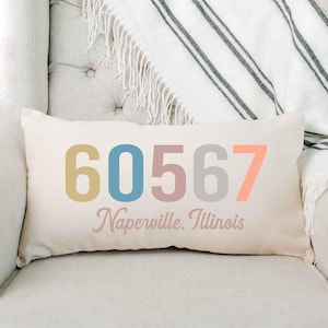 May include: A white rectangular pillow with the text "60567 Naperville, Illinois" printed in colorful letters. The numbers are in yellow, blue, pink, and gray.