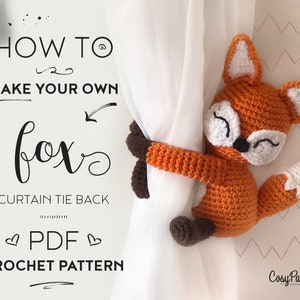Puede incluir: Un patrón de crochet para un sujetador de cortina en forma de zorro. El patrón está disponible para descargar en PDF. La imagen muestra un zorro de crochet sujetando un sujetador de cortina.
