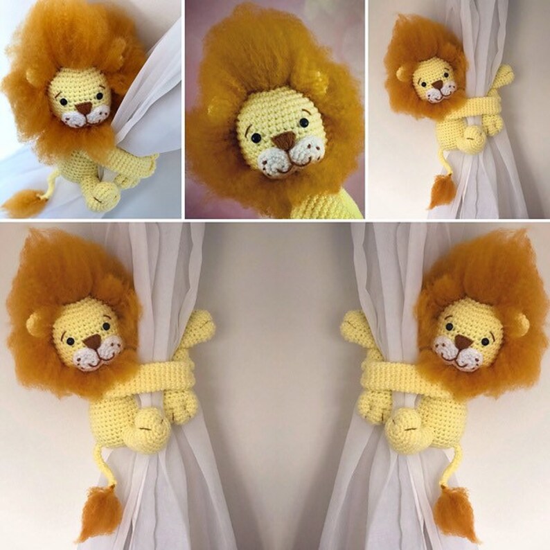 May include: Two crocheted lion curtain tiebacks in yellow and orange. The lions are holding onto white curtains with their paws.