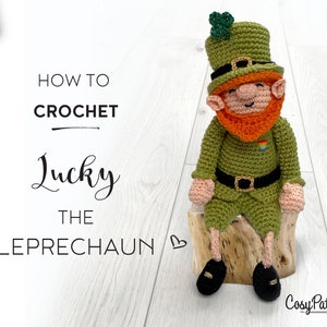 May include: How to Crochet Lucky the Leprechaun crochet pattern. A green crocheted leprechaun doll wearing a green hat with a shamrock on top, a green shirt, a gold belt, and black shoes. The leprechaun is sitting on a wooden stump.