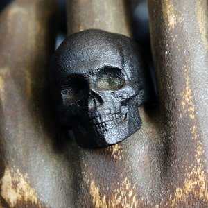 blackened steel skull ring on wooden carved hand front view