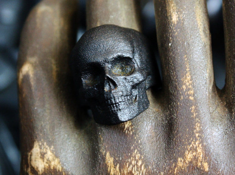 blackened steel skull ring on wooden carved hand front view