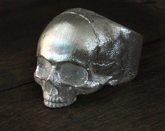 Può includere: Un anello a forma di teschio in argento con un design dettagliato. L'anello è in metallo e ha una finitura liscia e lucida.