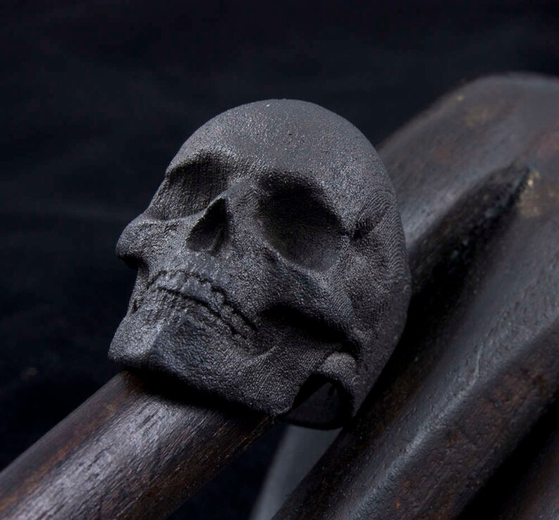 gothic blackened steel skull ring on wooden carved hand