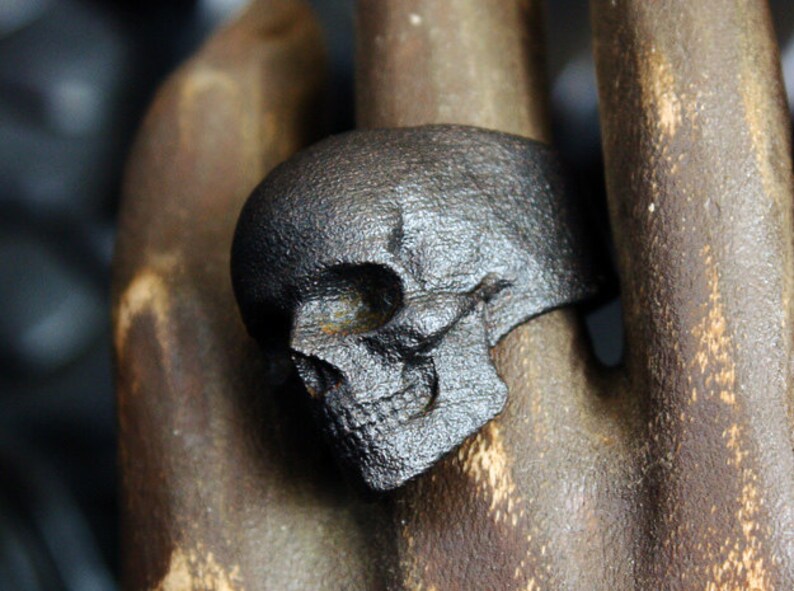 blackened steel skull ring on wooden carved hand side view