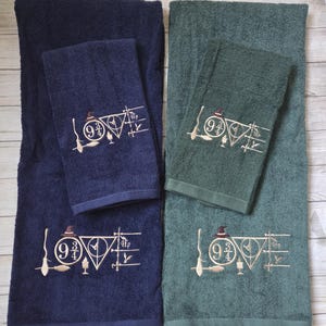 May include: A set of four towels in navy blue and dark green, each featuring an embroidered design that spells the word LOVE using thematic icons including a broomstick, the number 9 3/4, a triangle symbol, and a goblet in gold thread.