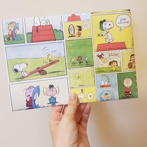 K&ouml;nnte beinhalten: Ein buntes Geschenkpapier mit Peanuts-Comicstrips mit Snoopy, Charlie Brown, Lucy und Woodstock. Das Papier hat einen gelben, gr&uuml;nen und roten Hintergrund mit schwarzen Umrissen. Der Text auf dem Papier lautet "Wing Walking!" und "Aaugh!"