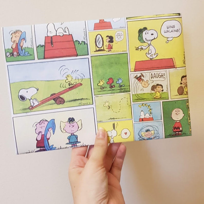 K&ouml;nnte beinhalten: Ein buntes Geschenkpapier mit Peanuts-Comicstrips mit Snoopy, Charlie Brown, Lucy und Woodstock. Das Papier hat einen gelben, gr&uuml;nen und roten Hintergrund mit schwarzen Umrissen. Der Text auf dem Papier lautet "Wing Walking!" und "Aaugh!"