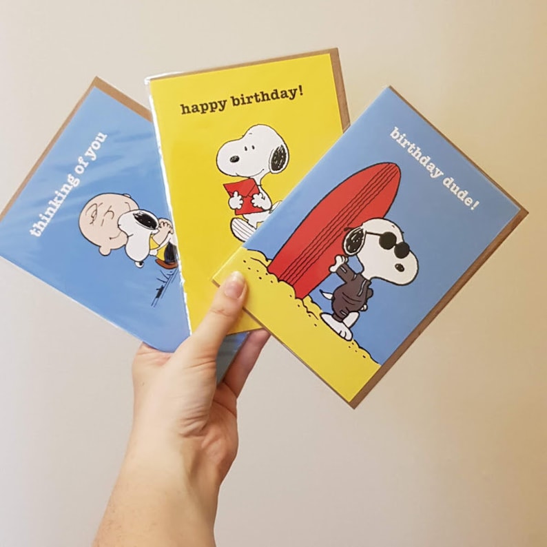 May include: Three greeting cards featuring Snoopy and Charlie Brown characters. One card says "thinking of you" on a blue background. Another says "happy birthday!" on yellow. The third says "birthday dude!" on blue.