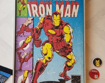 May include: A vintage comic book cover featuring Iron Man in a red and gold suit. The cover is titled "The Invincible Iron Man" and features the text "Framed for murder, Iron Man fights back against the man called HAMMER!"