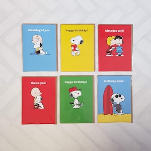 May include: Set of six greeting cards featuring Snoopy and Charlie Brown characters. The cards have various messages, including "thinking of you," "happy birthday," "thank you," and "birthday girl/dude." Each card has a different colored background, such as blue, yellow, and red.
