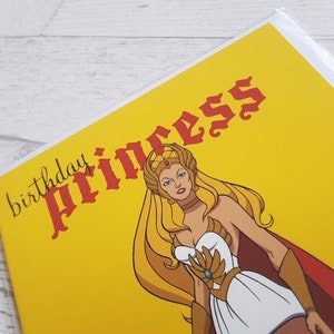 May include: A yellow birthday card with the text "birthday princess" in red and black lettering. The card features a cartoon image of a woman with long blonde hair wearing a white and gold costume.