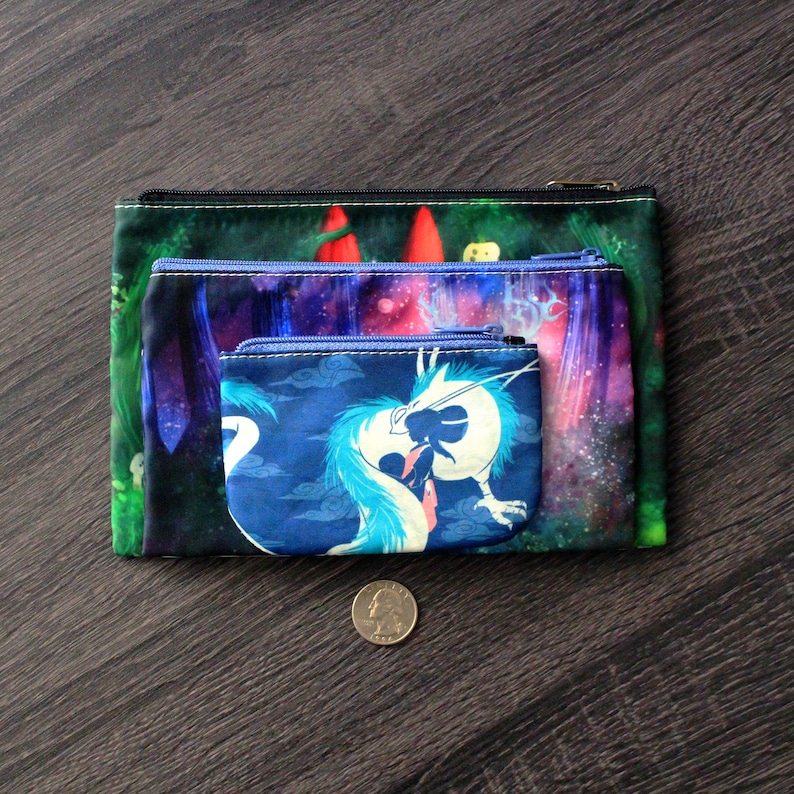 May include: Three zippered pouches with fantasy art. The largest pouch has a green forest scene, the middle pouch has a purple galaxy design, and the smallest pouch features a blue dragon. A coin is next to the pouches.
