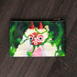 May include: A rectangular pouch featuring a vibrant illustration of a forest scene with a white, furry creature with a red mask and horns. Green vines and small white figures are also present. The pouch has a black zipper.