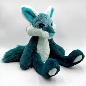 May include: A plush fox toy in shades of teal, white, and blue. The fox has a fluffy, soft texture, with a long tail and large ears. The toy is sitting with its legs outstretched, and its eyes are black.