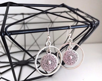 May include: Silver hoop earrings with a textured circular charm hanging from each hoop.