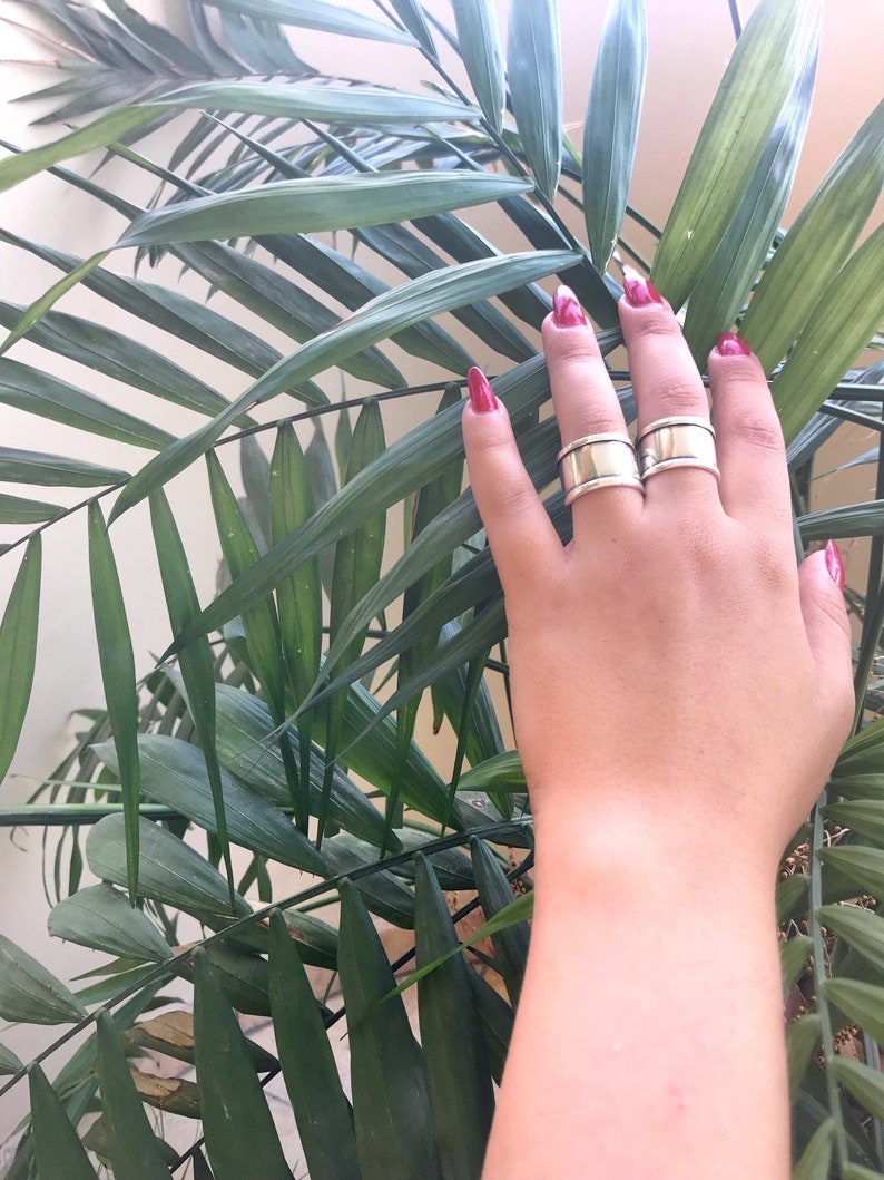 May include: Two silver rings on a hand with red nail polish. The hand is resting on a green plant with long leaves.