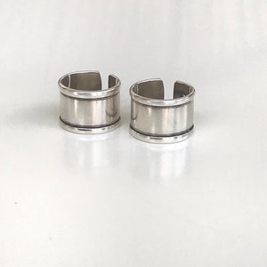 May include: Two silver rings with a wide band and a thin band around the top. The rings are made of metal and have a smooth finish.
