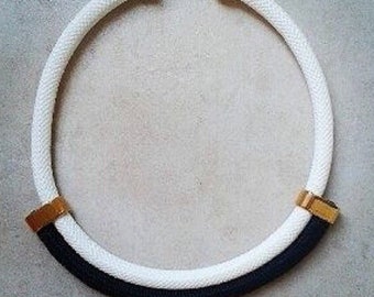 Puede incluir: Un collar de cuerda blanco y negro con detalles dorados. El collar está hecho de una cuerda gruesa y tiene un diseño simple.