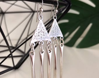 May include: Silver dangle earrings with a triangular pendant featuring a swirl design and five dangling spikes.