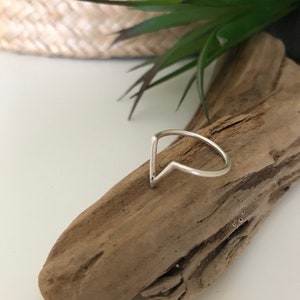 K&ouml;nnte beinhalten: Ein silberner Ring mit einem spitzen, V-f&ouml;rmigen Design. Der Ring liegt auf einem St&uuml;ck Treibholz.
