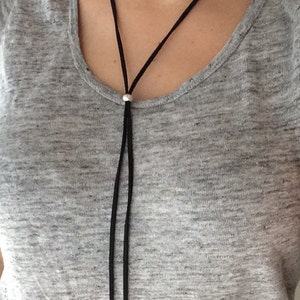 May include: A long black leather cord necklace with silver beads at the ends.