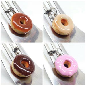 K&ouml;nnte beinhalten: Vier Miniatur-Donut-Anh&auml;nger mit unterschiedlich farbiger Glasur: Karamell, Hellrosa, Schokolade und Pfirsich. Jeder Donut hat ein Loch in der Mitte und einen silberfarbenen Verschluss zum Befestigen.