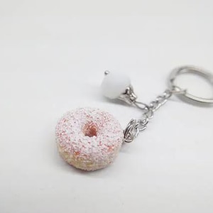 K&ouml;nnte beinhalten: Ein Schl&uuml;sselanh&auml;nger in Donut-Form mit rosa Zuckerguss und wei&szlig;en Streuseln. Der Schl&uuml;sselanh&auml;nger hat eine silberne Kette, eine wei&szlig;e Perle und einen silbernen Schl&uuml;sselring. Der Donut ist eine Miniatur.
