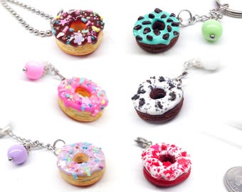 May include: A collection of miniature donut keychains in various colors. Each donut features colorful frosting and sprinkles, with a silver chain and a decorative bead. The donuts are in shades of brown, pink, white, and red.