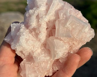 May include: A large, pink Himalayan salt crystal cluster with a rough, textured surface. The crystal is made up of many smaller, cubic crystals that are clustered together.
