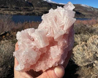 May include: A large, pink Himalayan salt crystal cluster with a rough, natural texture. The crystal is composed of many smaller, cubic crystals that are intergrown together. The crystal has a translucent, slightly pink color.