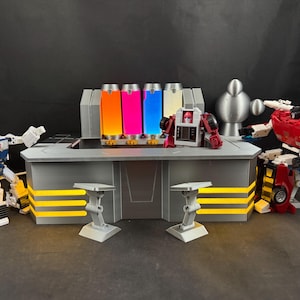 May include: A gray and yellow futuristic-themed display with colorful glowing cylinders, and several toy robots. The display has a gray countertop and two small gray stands. The robots are in various colors.