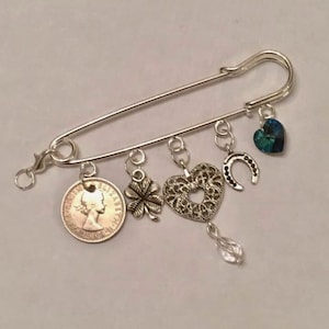 May include: Silver safety pin charm bracelet with a coin, a four-leaf clover, a heart, a horseshoe, and a crystal charm.