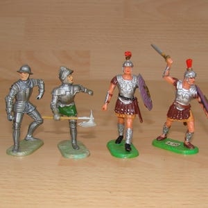 May include: Four toy soldier figurines, two in silver armour, one in red and silver armour, and one in brown and silver armour. The figures are standing on green bases.
