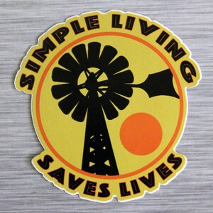 May include: A die-cut sticker with a yellow background and a black windmill illustration. The sticker has a circular design with the words "SIMPLE LIVING" and "SAVES LIVES" in a semi-circular arrangement. An orange sun is also featured.