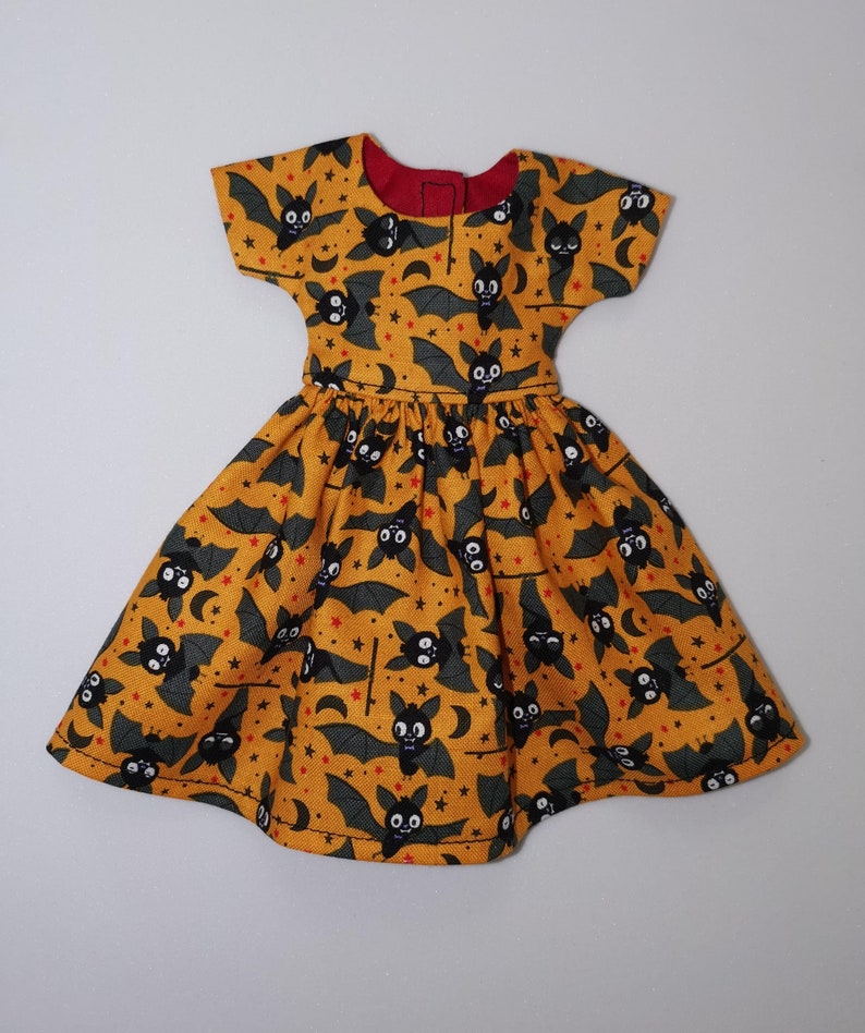May include: A yellow dress with a black bat print. The dress has short sleeves and a gathered skirt.