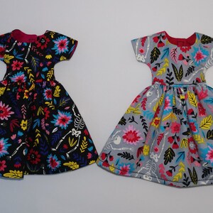 May include: Two doll dresses with a floral and skeleton print. One dress is black with pink, yellow, and blue flowers. The other dress is gray with pink, yellow, and blue flowers.