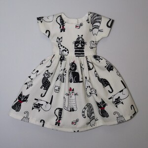 May include: A white dress with a black and white cat print. The dress has short sleeves and a full skirt.