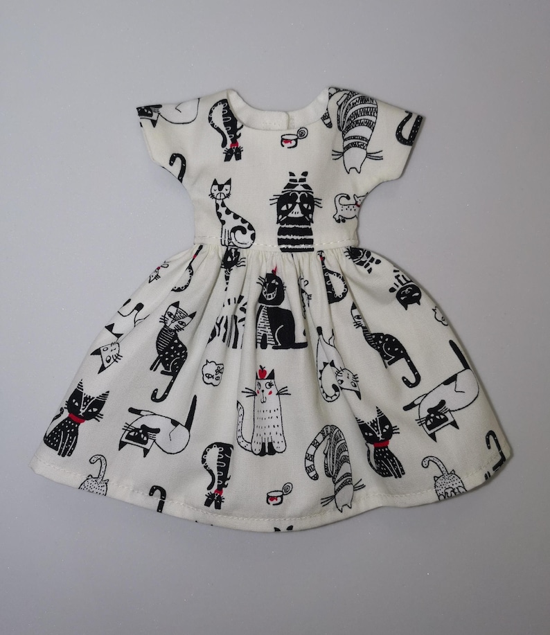May include: A white dress with a black and white cat print. The dress has short sleeves and a full skirt.