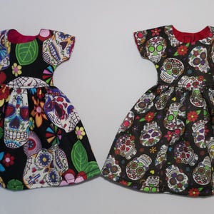 May include: Two black dresses with colorful sugar skull patterns. The dresses have short sleeves and a gathered skirt.