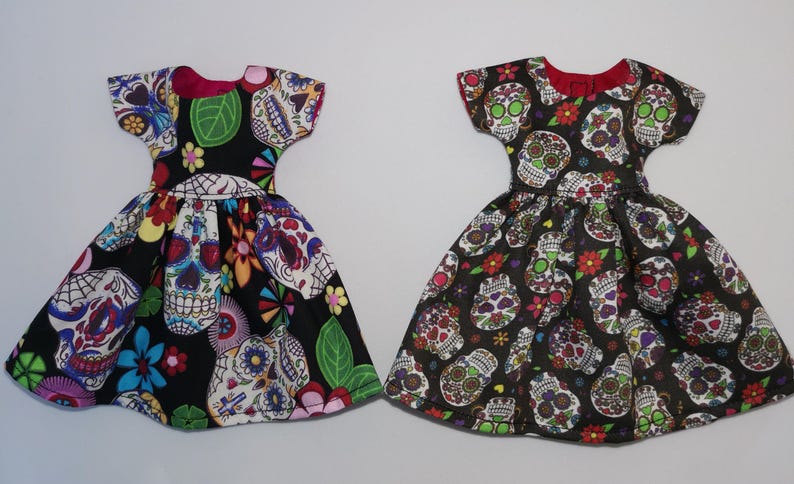 May include: Two black dresses with colorful sugar skull patterns. The dresses have short sleeves and a gathered skirt.