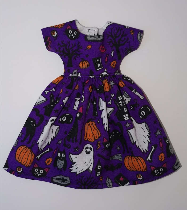 May include: A purple dress with a Halloween print featuring black cats, ghosts, pumpkins, and other spooky elements.